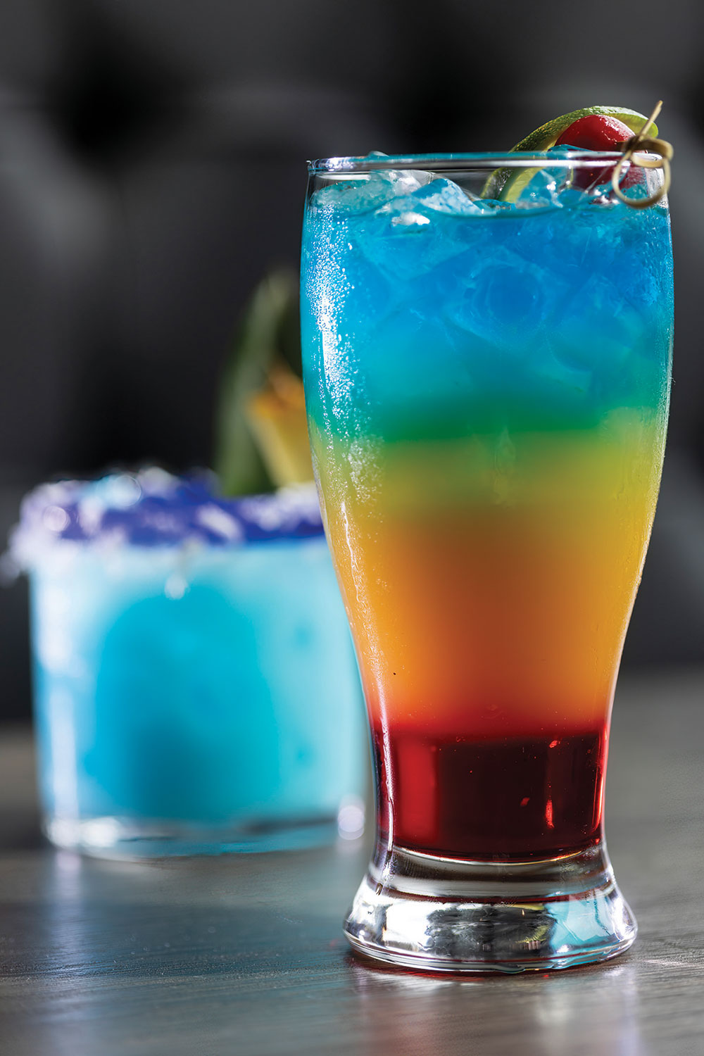 The Rainbow Paradise cocktail layers blue curacao liqueur, rum, pineapple juice, and grenadine syrup.